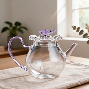 May include: A clear glass teapot featuring a purple handle and a purple flower-shaped knob on the lid. The teapot has a rounded body, a curved spout, and a scalloped rim design around the top opening, all crafted from transparent glass material.