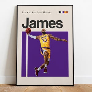 Könnte beinhalten: Poster mit einem Basketballspieler in einem gelb-violetten Trikot, der sich mit einem Basketball in der Luft befindet. Der Name "James" steht über dem Spieler. Der Hintergrund ist lila mit weißen und schwarzen Akzenten. Das Poster ist schwarz gerahmt.