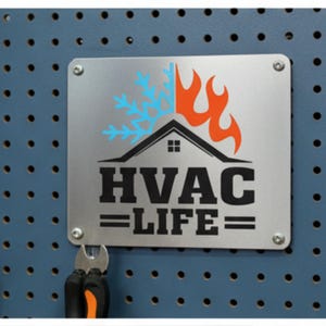 May include: A silver metal sign with the words "HVAC LIFE" in bold black letters. The sign features a graphic of a house with a flame and snowflake design. The sign is mounted on a blue pegboard with tools.