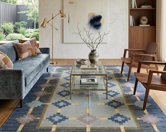May include: A rectangular area rug featuring a geometric pattern in shades of deep blue, light blue, and gold. The design consists of a central light blue panel framed by a dark blue border, accented with repeating diamond shapes in muted pink and gold.