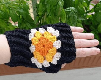 May include: Black crocheted fingerless glove with a colourful floral design. The flower features orange, yellow, and white petals. The glove is worn on a hand, showcasing the intricate crochet work and colour contrast.