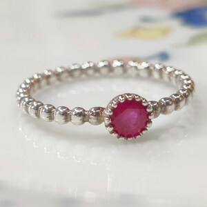 May include: A silver ring featuring a beaded band and a central, round, bright pink gemstone. The gemstone is set in a scalloped bezel. The ring is displayed on a white surface.