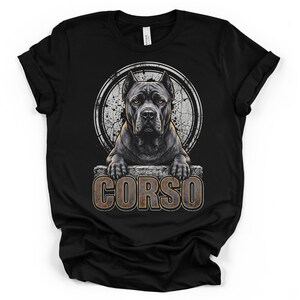 Puede incluir: Una camiseta negra con una ilustración gráfica de un perro Cane Corso de ojos ámbar. El perro está situado detrás de un borde con textura de piedra con la palabra CORSO impresa en letras grandes y desgastadas debajo, dentro de un marco circular.
