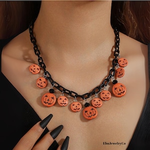 Könnte beinhalten: Schwarze Kettenhalskette mit orangefarbenen Kürbisanhängern. Die Halskette hat kleine, lächelnde Kürbisanhänger, ideal für Halloween. Ein festliches Accessoire.