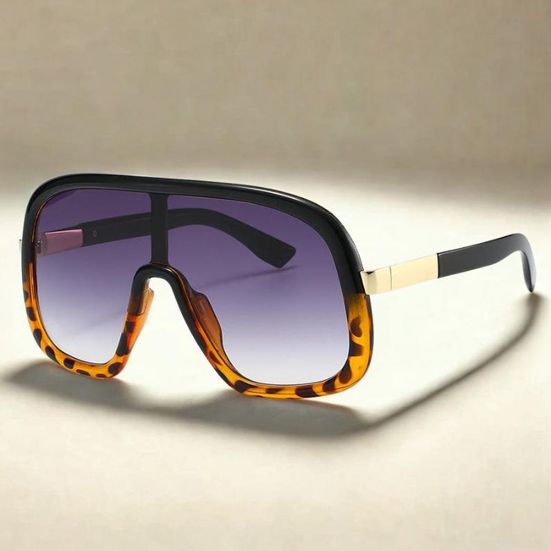 May include: Oversized sunglasses with a black frame and gradient purple lenses. The lower frame has a tortoise shell pattern. The temples are black with a gold accent. A stylish accessory for sun protection.
