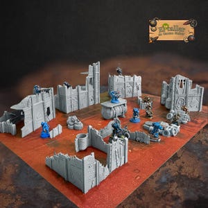 Könnte beinhalten: Ein Tabletop-Geländeset mit grauen, modularen Gebäuderuinen und Miniaturfiguren. Das Set enthält Mauern, Strukturen und Fahrzeuge, die auf einer rot-braunen Oberfläche angeordnet sind. Die Miniaturen sind in Blau und Braun bemalt.
