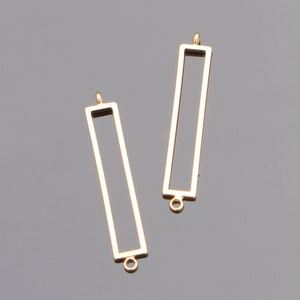 May include: Two gold-colored metal rectangular frames with a loop at the top and bottom. The frames are empty and ready to be filled with resin or other materials.