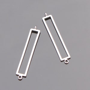 May include: Two silver metal rectangular frames with a loop at the top and bottom. The frames are empty and ready to be filled with resin or other materials.