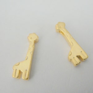 May include: Two gold-colored giraffe charms with a textured surface. The charms are small and would be suitable for jewelry making or other craft projects.