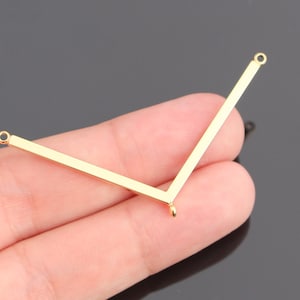 May include: A gold-toned metal V-shaped jewelry connector component featuring a smooth, flat surface. The piece has a small circular loop at each of the two top ends and a single, smaller circular loop centered at the bottom point of the V-shape.