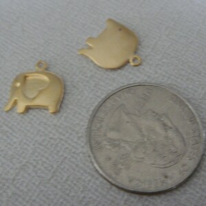 May include: Two gold-colored metal charms, one shaped like an elephant and the other shaped like a pig, next to a US quarter.