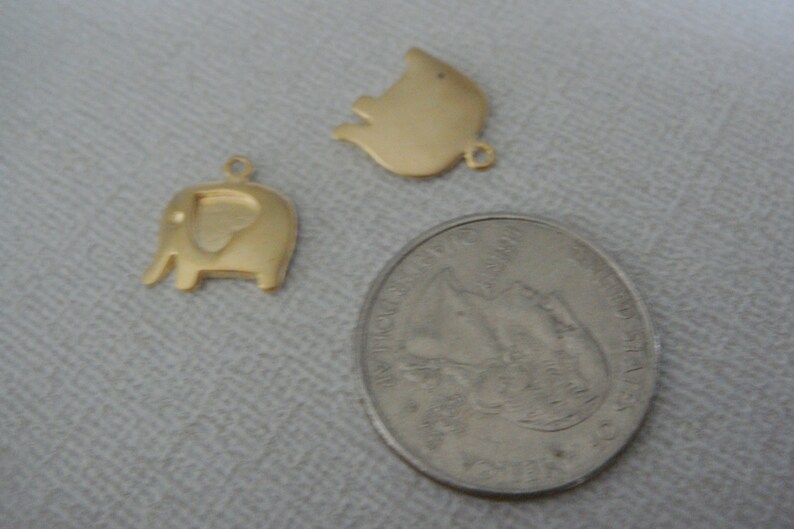 May include: Two gold-colored metal charms, one shaped like an elephant and the other shaped like a pig, next to a US quarter.