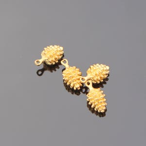 May include: Three gold-coloured metal pine cone charms with a loop at the top for attaching to jewellery or other crafts.