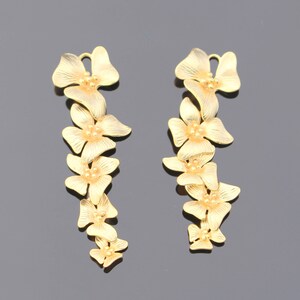 May include: A pair of gold-tone earrings with a floral design. Each earring features a chain of five flowers, each with a small, round center.
