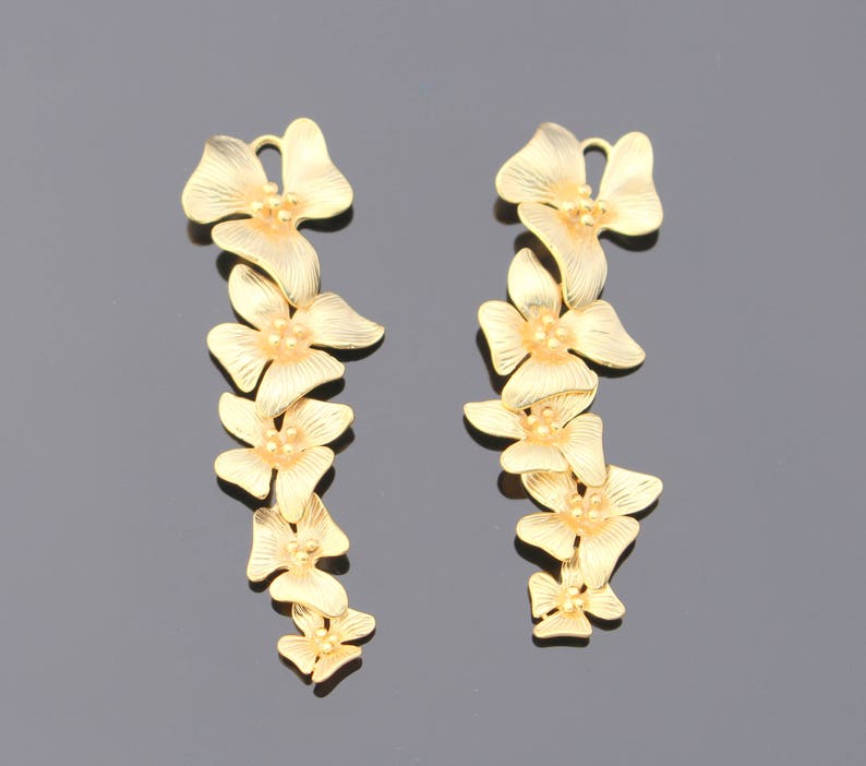 May include: A pair of gold-tone earrings with a floral design. Each earring features a chain of five flowers, each with a small, round center.