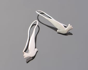 May include: A pair of silver dove earrings. The doves are in flight and are made of a smooth, shiny metal.