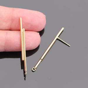 May include: A pair of gold-toned earring findings with a straight bar design. One earring has a single bar, while the other has three bars stacked on top of each other.
