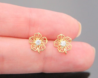 Könnte beinhalten: Ein Paar goldene Ohrringe in Blumenform mit einem kleinen, klaren Strassstein in der Mitte jeder Blume.