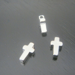 May include: Three silver charms: two cross shapes and one rectangular charm with a loop at the top.
