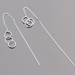 May include: A pair of silver dangle earrings with three interlocking circles on each earring.