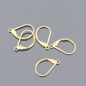 May include: Four gold-toned earring hooks, also known as ear wires, are arranged on a gray surface. The hooks are made of metal and have a simple, classic design.