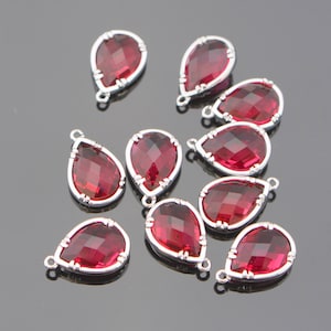 May include: Ten silver teardrop-shaped pendants with red crystal accents. Each pendant has a loop at the top for attaching to a chain or cord.