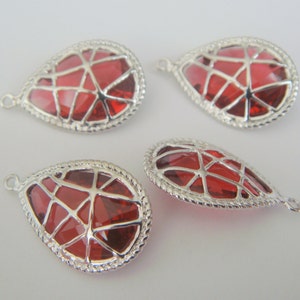 May include: Four red glass teardrop-shaped pendants with silver metal frames and a wire design. Each pendant has a loop for hanging.