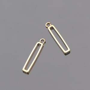 May include: Two gold-colored, rectangular pendant charms with a hollow center and a small loop at the top. The charms are displayed on a gray surface. These charms are suitable for jewelry making, such as earrings or necklaces.