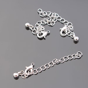 Puede incluir: Dos extensores de cadena plateados con cierres de langosta y tapas de bola. Los extensores miden aproximadamente 5 cm de largo.