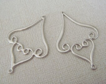 May include: Two silver metal charms shaped like a heart with a swirl design. The charms have a loop at the top for attaching to a necklace or bracelet.