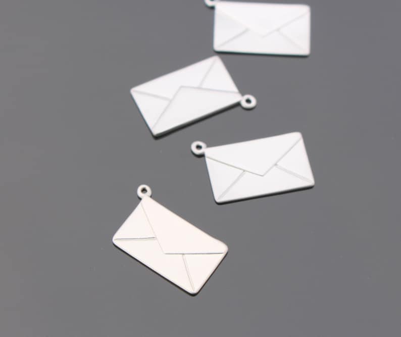 May include: Several silver-colored envelope charms with a loop at the top for jewelry making. The charms are rectangular with a detailed envelope design. The background is a solid gray color.