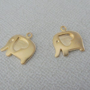 May include: Two gold-colored elephant charms with a heart-shaped cutout in the center. The charms have a loop at the top for attaching to a necklace or bracelet.