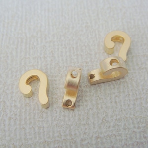 Könnte beinhalten: Vier goldfarbene Metallhaken mit einem dekorativen Design. Die Haken haben ein kleines Loch oben und ein größeres Loch unten.