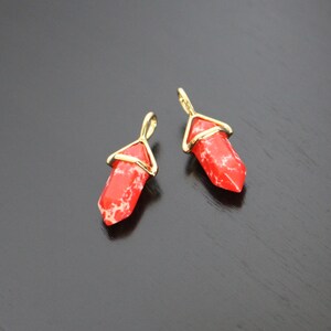 May include: Two red and white gemstone pendants with gold wire accents. The pendants are shaped like a long, thin point.