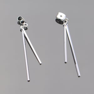 May include: A pair of silver dangle earrings with two thin, straight bars extending from the earring hook.