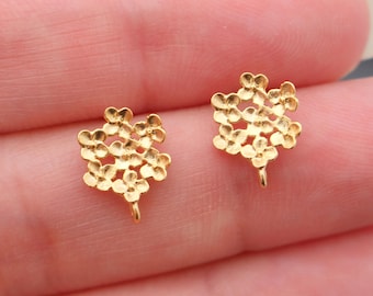May include: Two gold-colored floral-shaped earring components. Each component features a cluster of small, detailed flower shapes. The earrings have a small loop at the bottom for attachment. The earrings are held in a person's hand.