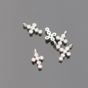 May include: Four silver cross charms with clear crystal accents. Each charm has a loop for attaching to a necklace or bracelet.