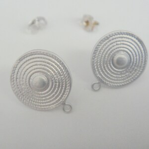 Puede incluir: Un par de pendientes de plata con un diseño circular que presenta círculos concéntricos. Los pendientes tienen un estilo simple y elegante.