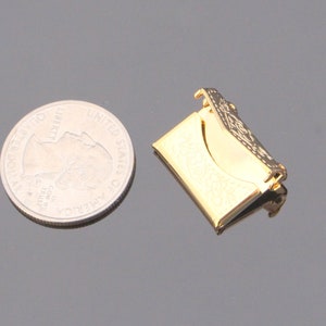 May include: A gold-colored metal envelope clasp with an ornate design. The clasp is about the size of a US quarter.