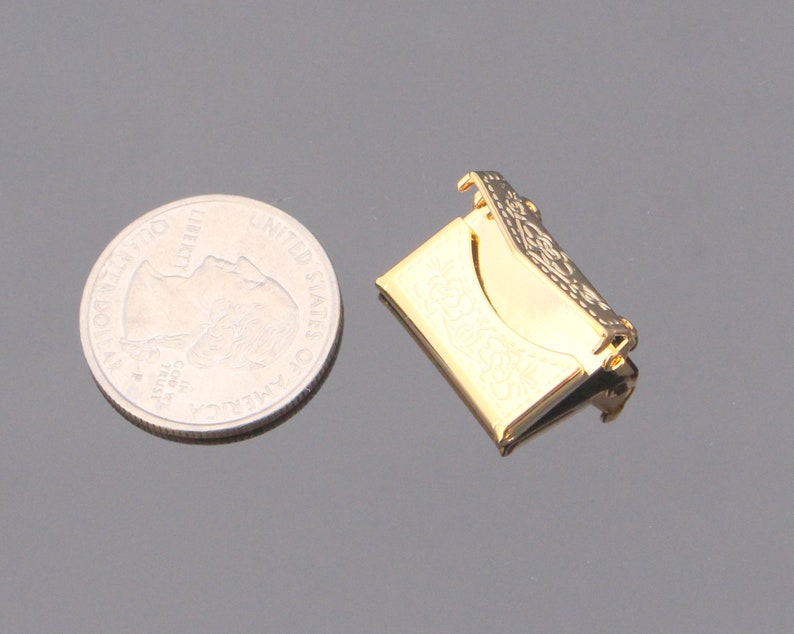 May include: A gold-colored metal envelope clasp with an ornate design. The clasp is about the size of a US quarter.