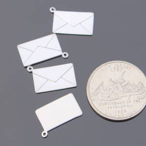 May include: A collection of silver-colored envelope charms and a quarter coin. The charms are small, detailed replicas of envelopes, each with a loop for attaching to jewelry or other crafts. The quarter features an image of a historical scene.