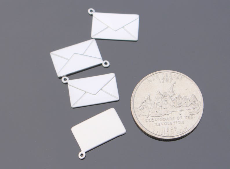 May include: A collection of silver-colored envelope charms and a quarter coin. The charms are small, detailed replicas of envelopes, each with a loop for attaching to jewelry or other crafts. The quarter features an image of a historical scene.