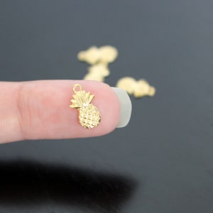 May include: Gold pineapple charm with a detailed design. The charm is small and perfect for adding a tropical touch to jewelry or crafts.