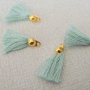 May include: Four light green tassels with gold metal loops. The tassels are made of soft, fluffy yarn and are perfect for adding a touch of whimsy to any project.