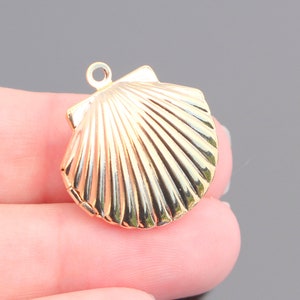 May include: Gold-toned seashell charm pendant with a detailed, textured design. The pendant has a loop at the top for attaching to a necklace or bracelet.