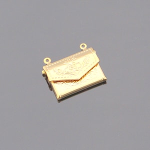 May include: Gold-toned metal charm in the shape of a small, ornate envelope with a floral design. The charm has two loops at the top for attaching to a necklace or bracelet.