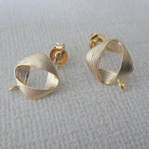 May include: A pair of gold-toned earrings with a twisted, textured design. The earrings have a loop at the bottom for attaching charms or pendants.