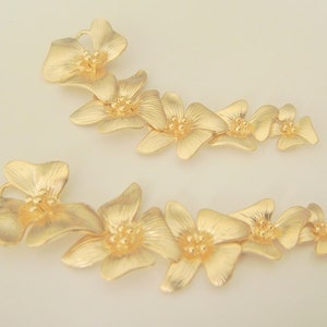 May include: Two gold-toned flower-shaped hair clips. Each clip features a series of five connected flowers with a textured surface.