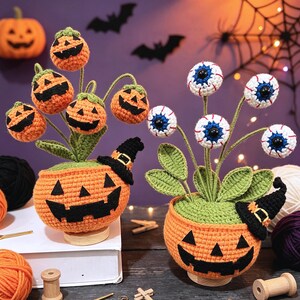 Puede incluir: Dos decoraciones de Halloween tejidas a ganchillo con macetas naranjas en forma de calabaza, caras de jack-o'-lantern negras y pequeños sombreros de bruja. Una maceta tiene tallos de calabaza y la otra tallos con globos oculares.