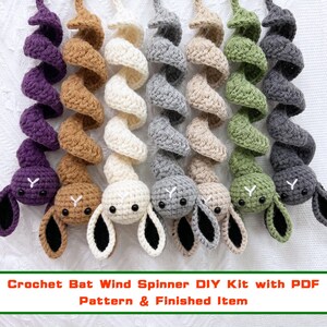 May include: A set of seven spiral-shaped crochet bat ornaments in purple, tan, cream, light grey, beige, olive green, and dark grey. Each bat features a long, coiled body, two black bead eyes, a white stitched nose, and two pointed ears.